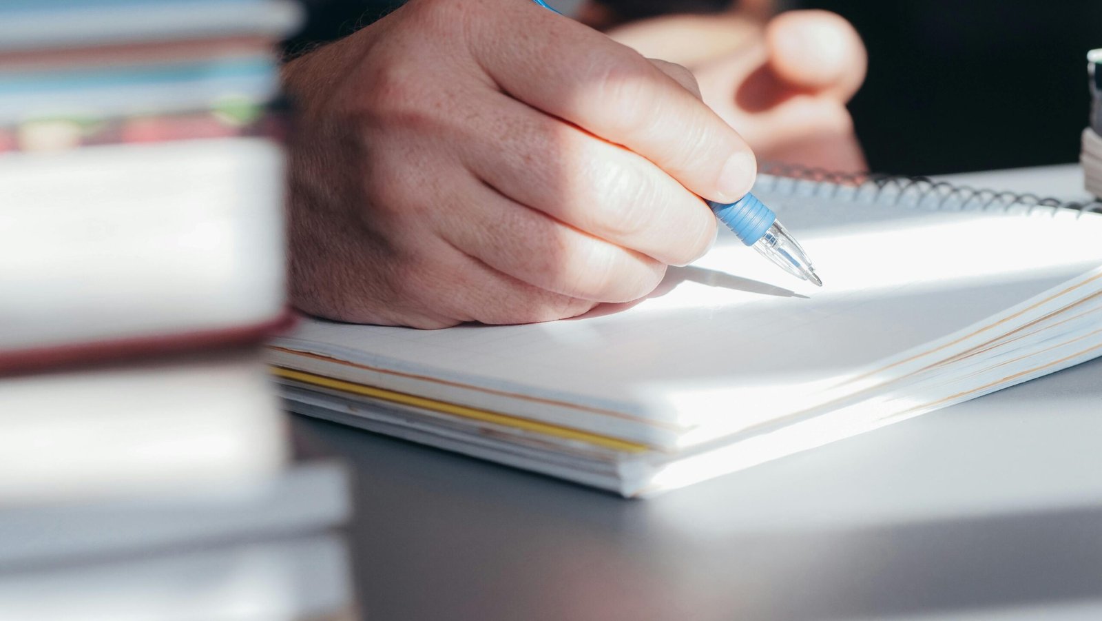 A person writing notes with a pen in a bright, indoor setting.