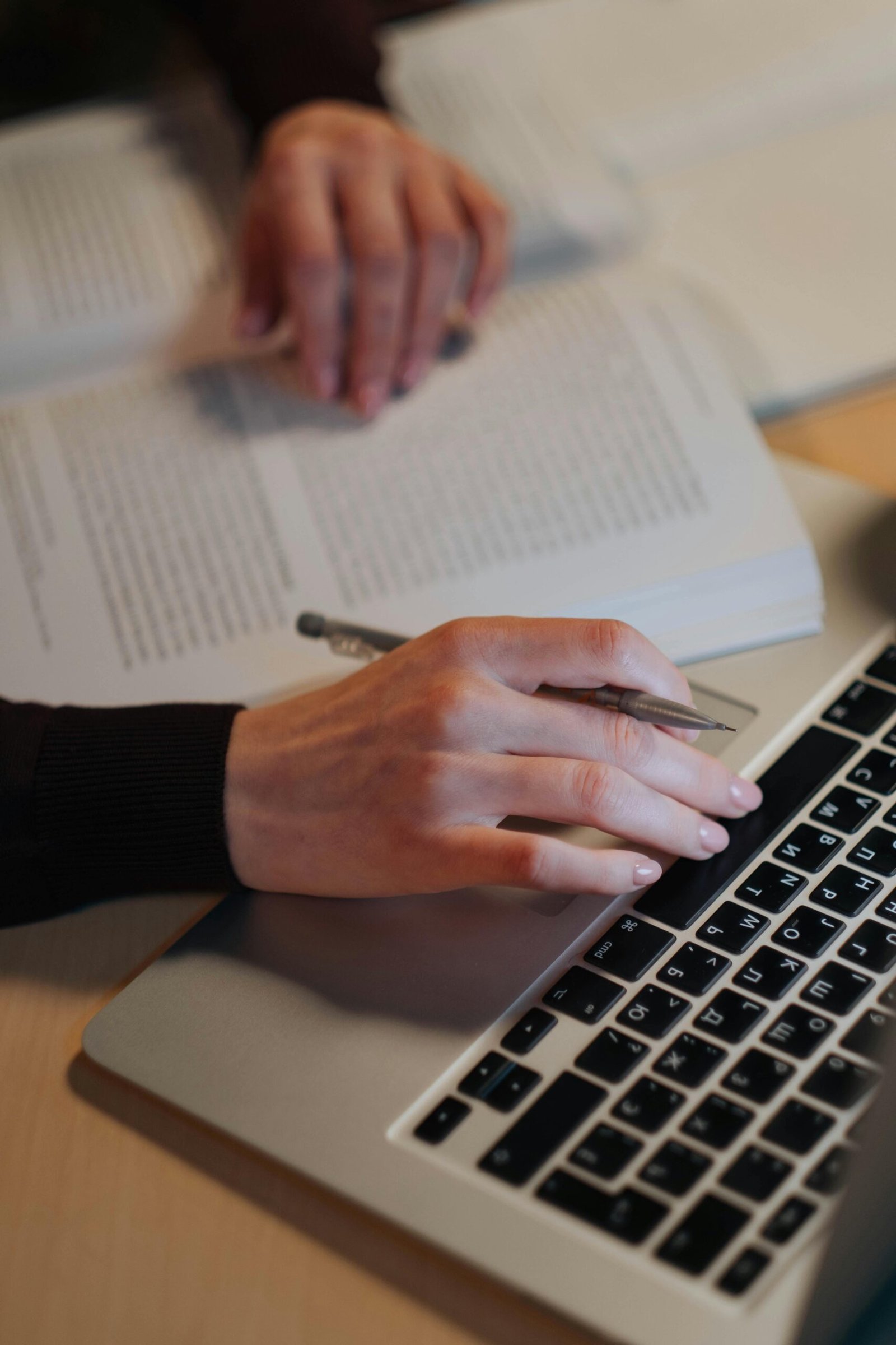 Close-up of hands writing notes on a laptop and book indoors.